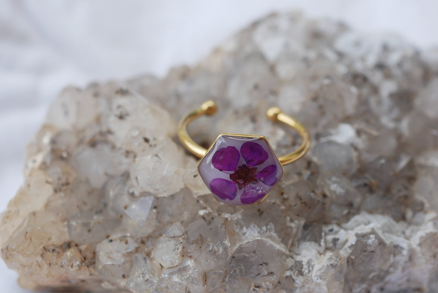 A ring with a purple flower design rests on a rock.