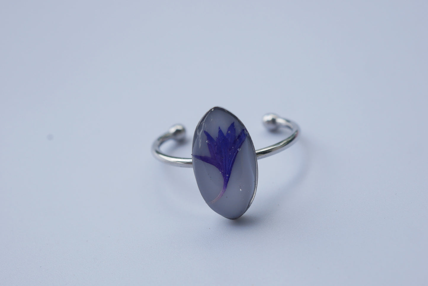 A silver ring with a purple flower design on it, resting on a plain white surface.