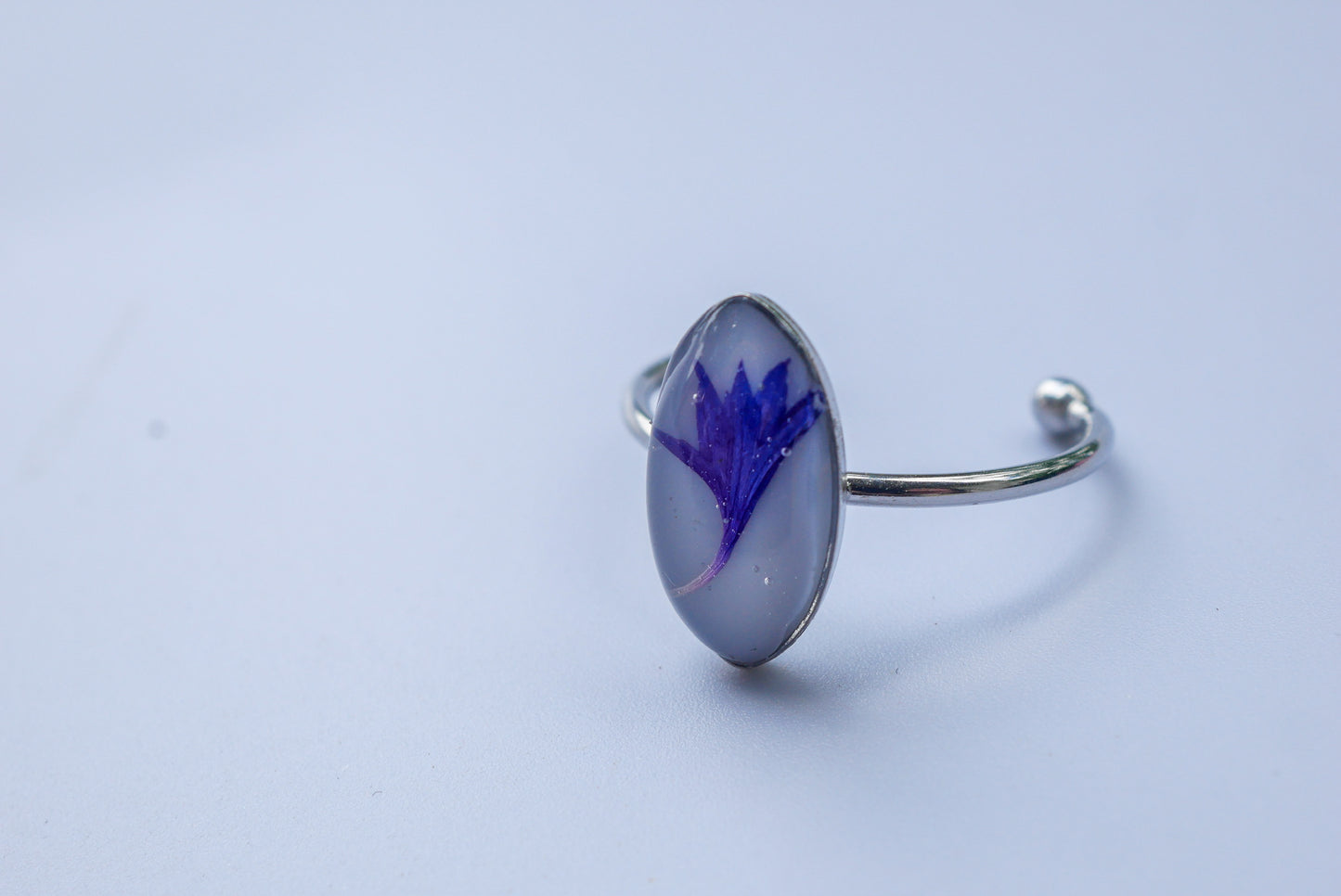 A silver cuff bracelet with a round, oval-shaped stone featuring a blue flower design.