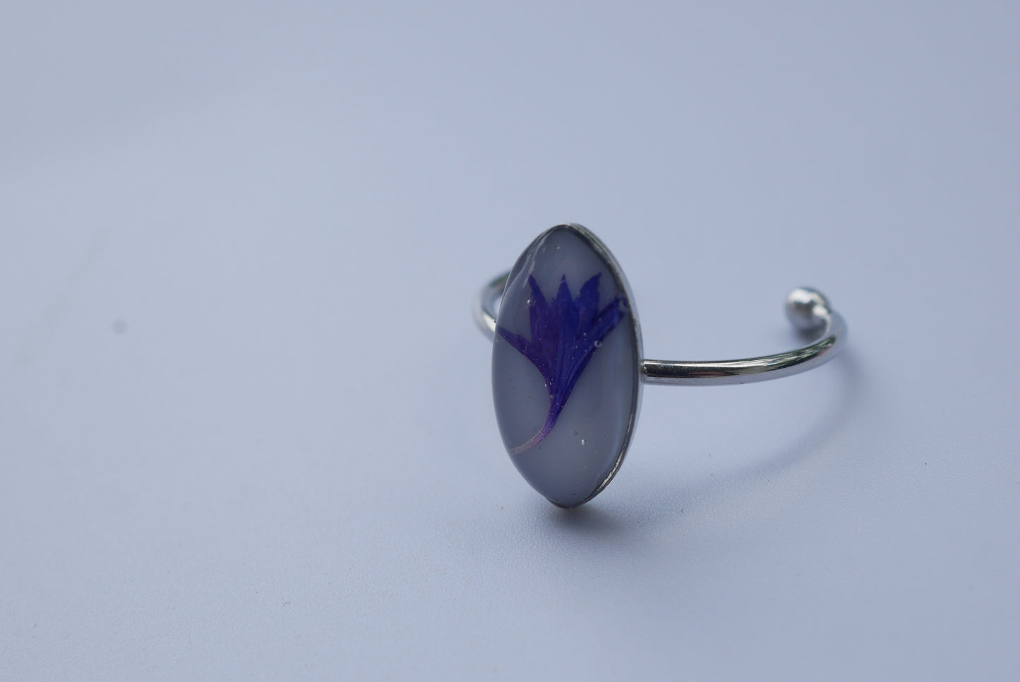 A silver cuff bracelet with a blue flower design on it, resting on a plain white surface.