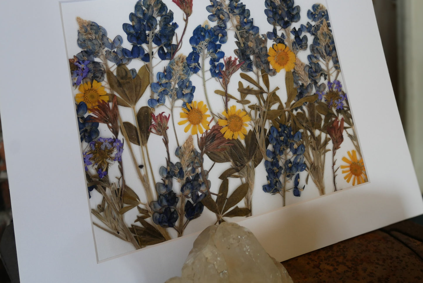 The image is a framed print featuring a vibrant arrangement of dried flowers, including sunflowers and blue flowers, creating a colorful and visually appealing display.