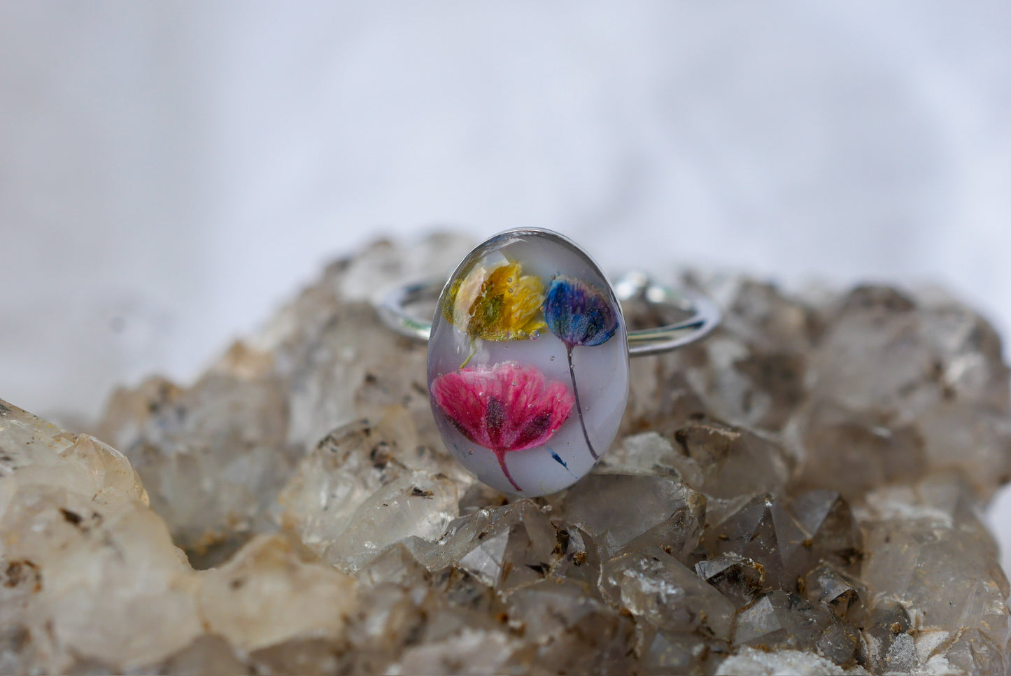 A ring with a clear, oval-shaped design featuring colorful flowers is placed on a rock formation.