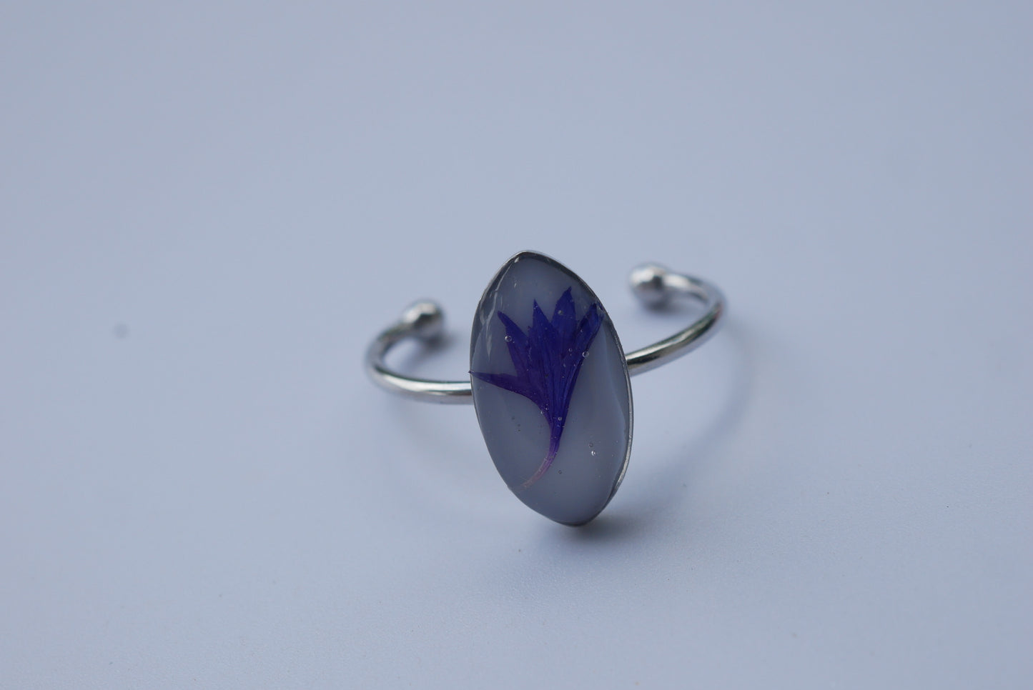 A silver ring with a blue flower design on it, resting on a plain surface.