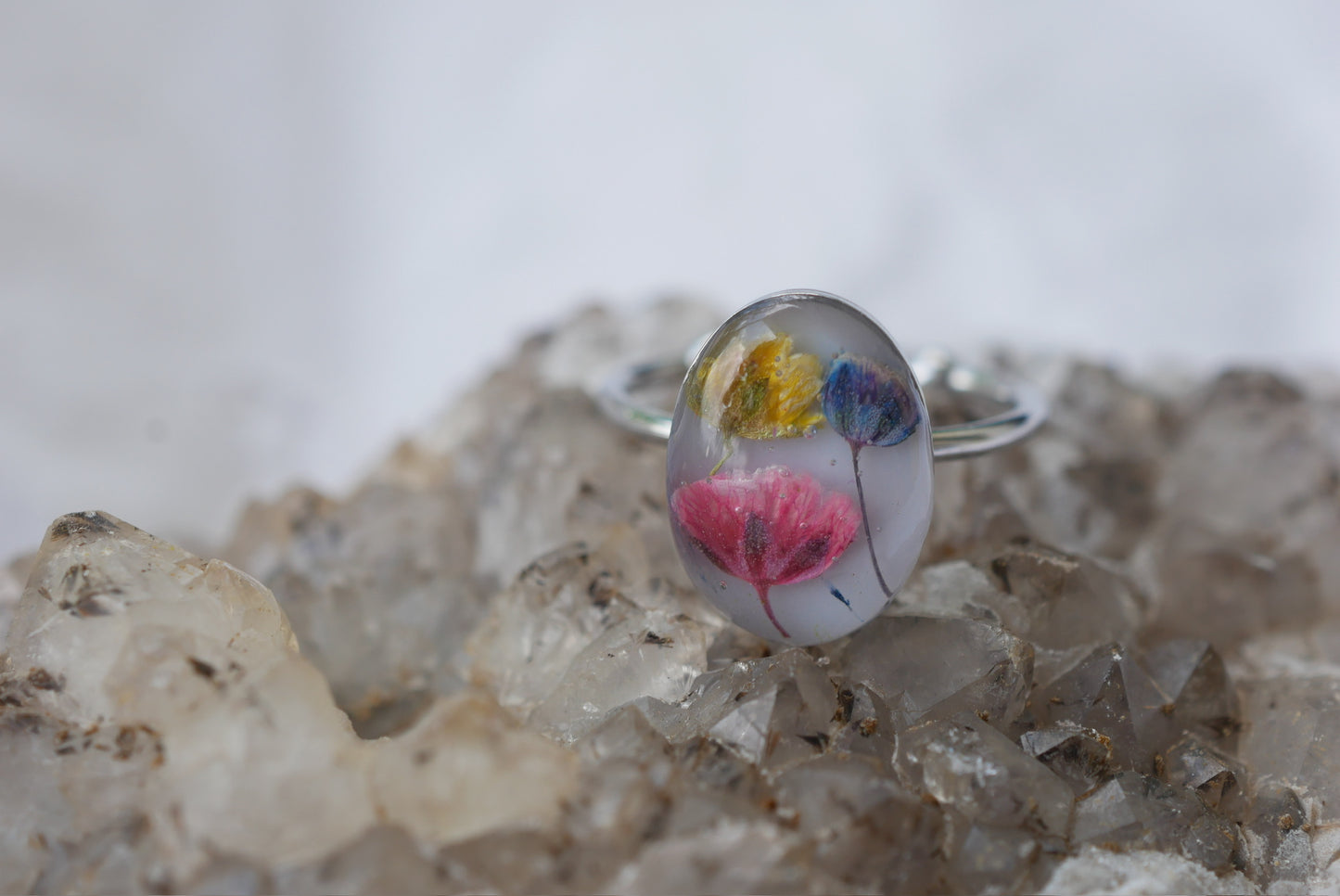 A ring with a clear, oval-shaped design featuring colorful flowers is placed on a bed of crystals.