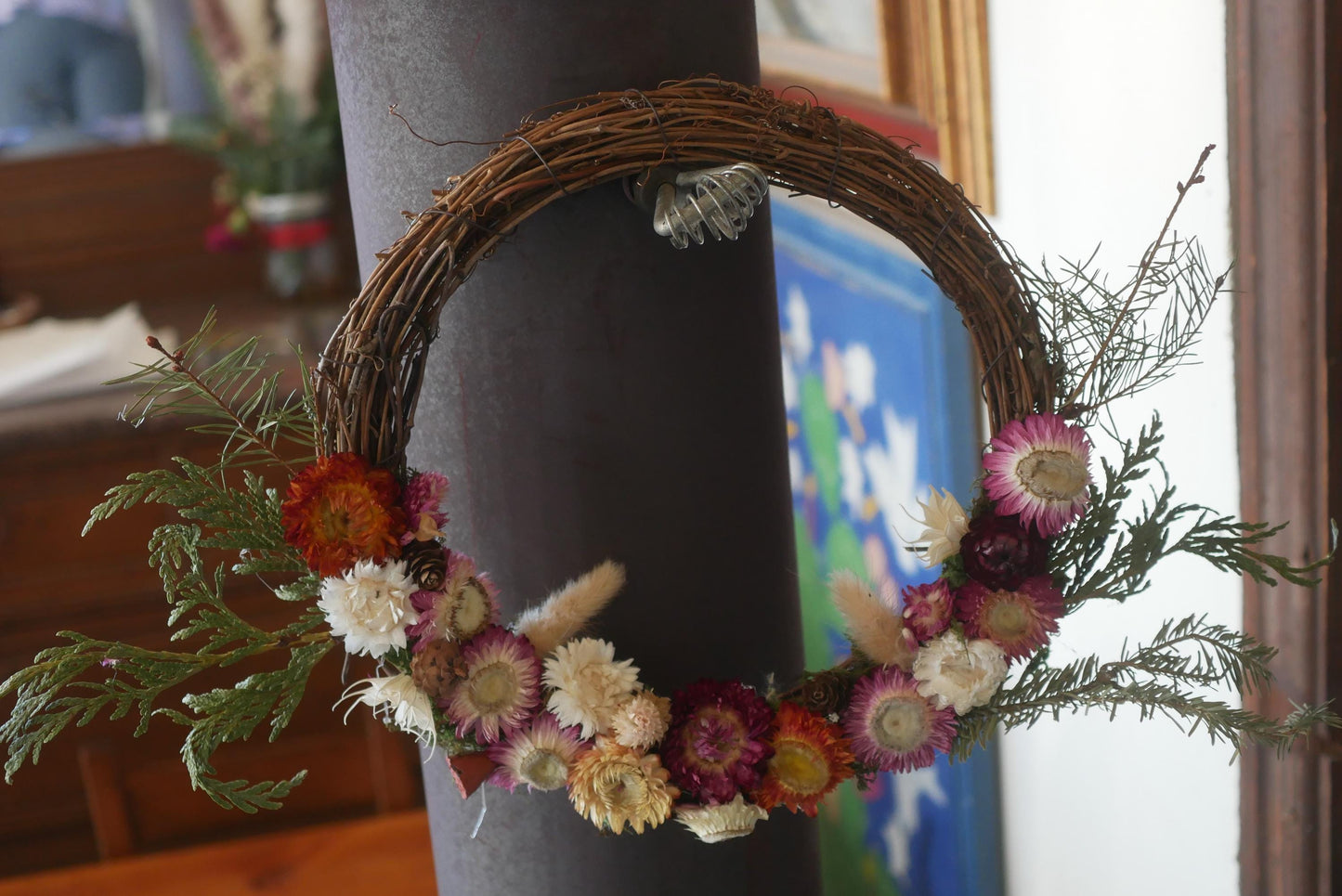 A wreath made of dried flowers and greenery is hanging on a dark pole.