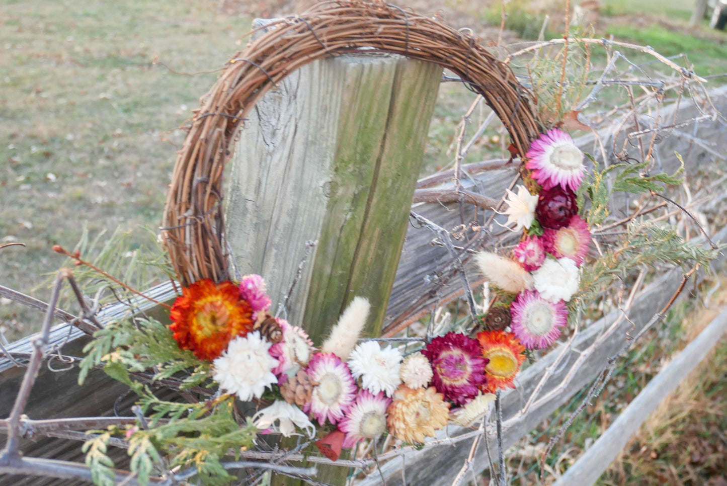 A wreath made of twigs and flowers is hanging on a wooden fence.