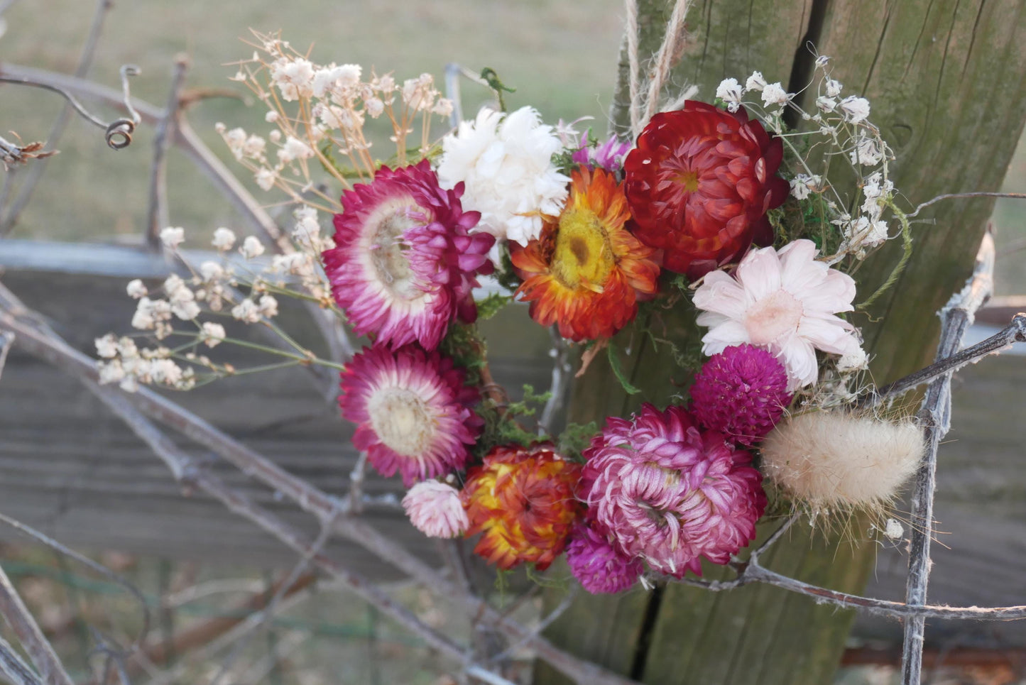 A vibrant bouquet of colorful flowers, including red, pink, white, and orange blooms, is displayed on a wooden post.