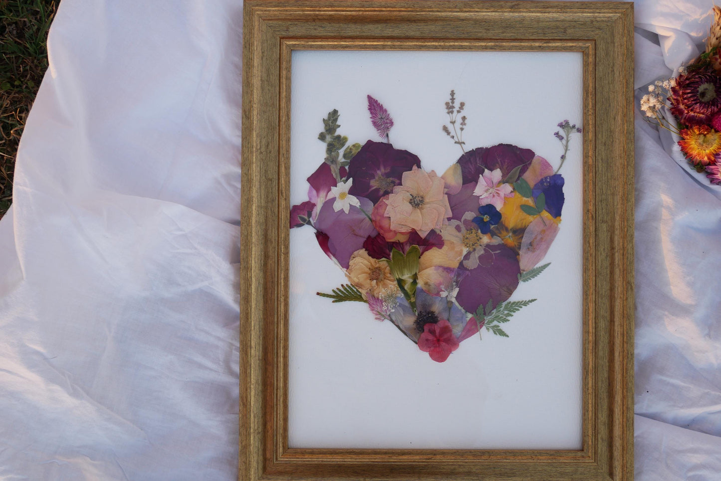 A framed collage of various colorful flowers, including purple, pink, yellow, and white flowers, arranged in the shape of a heart.