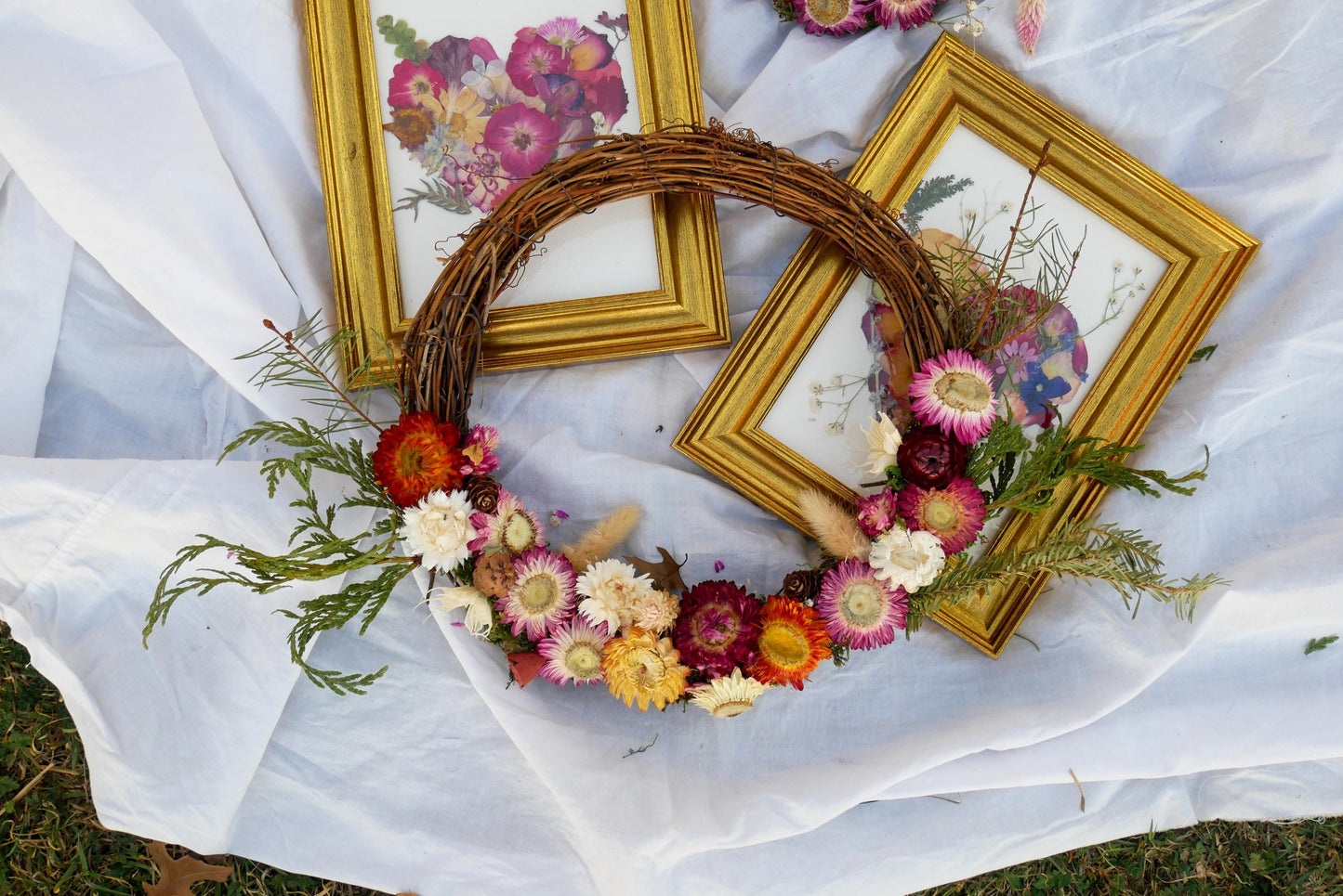 a wreath made of flowers and greenery, placed on a white cloth. The wreath is surrounded by three framed pictures, creating a decorative arrangement.