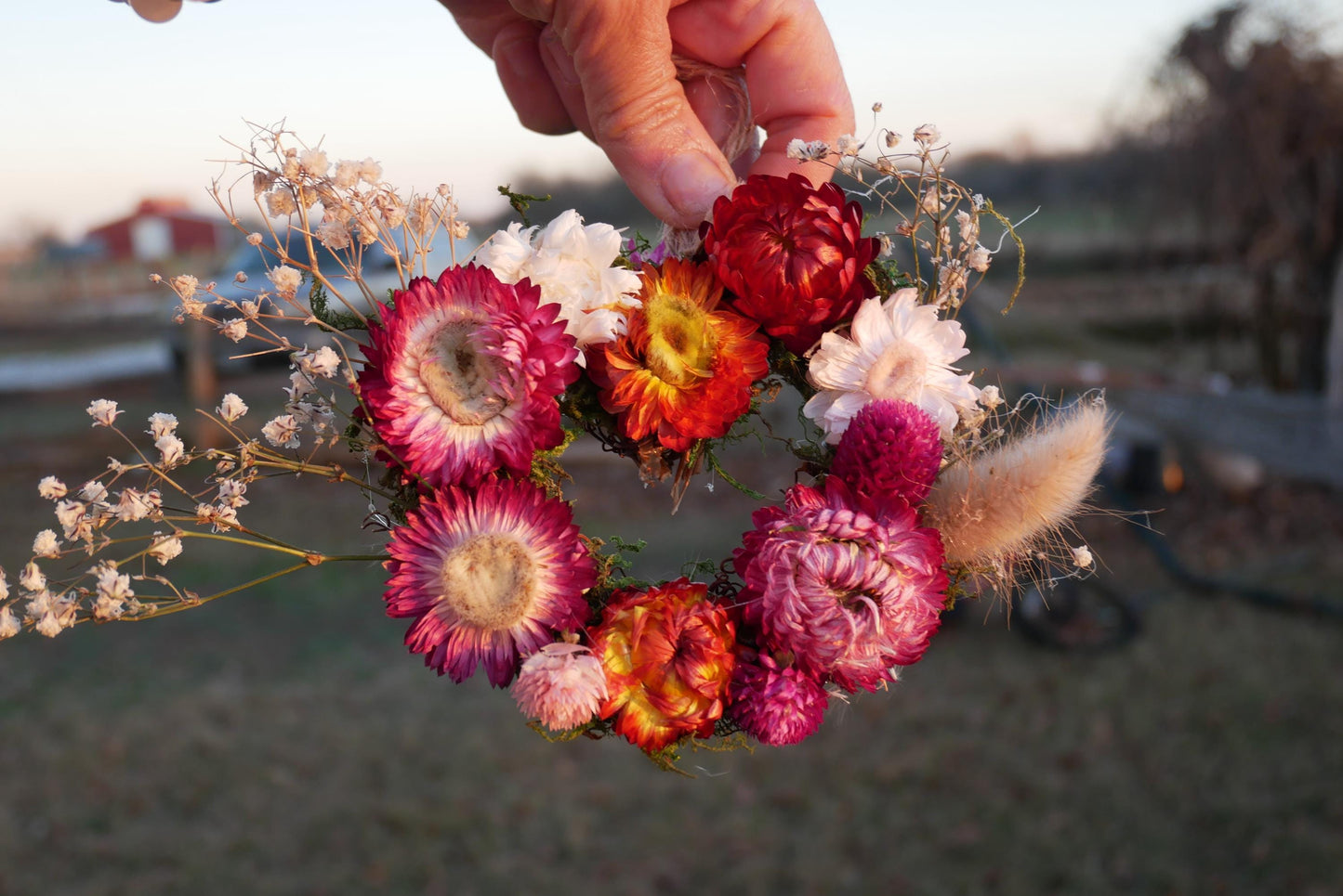 A hand holds a vibrant floral arrangement, featuring a variety of colorful flowers including red, orange, and pink blooms, as well as delicate white and purple flowers.