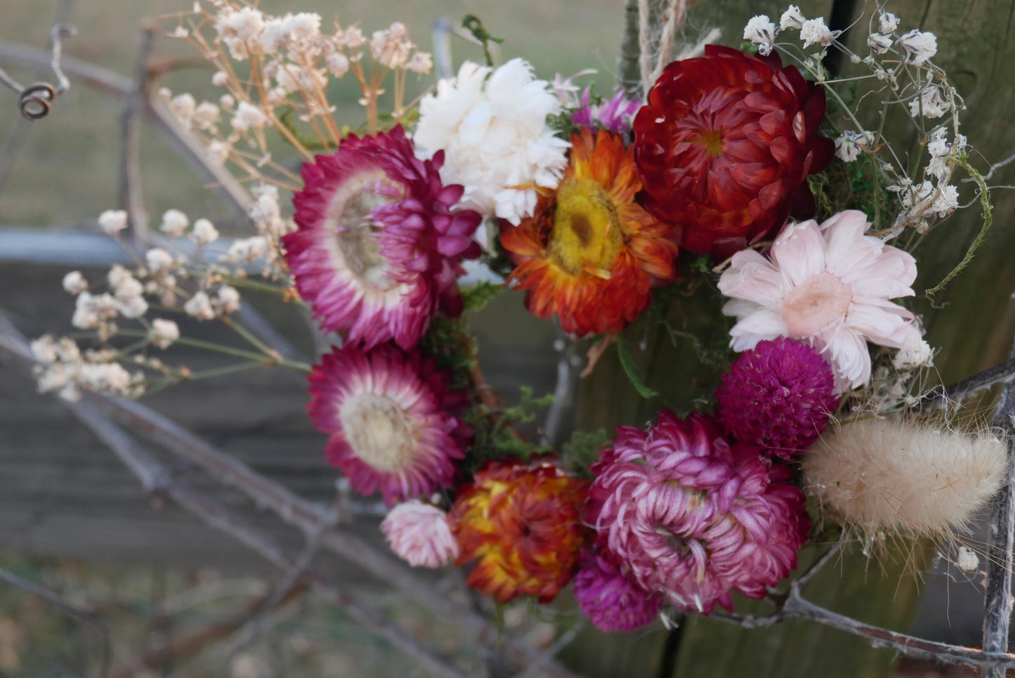 A vibrant bouquet of various colorful flowers, including red, pink, orange, and white blooms, is displayed against a blurred natural background.