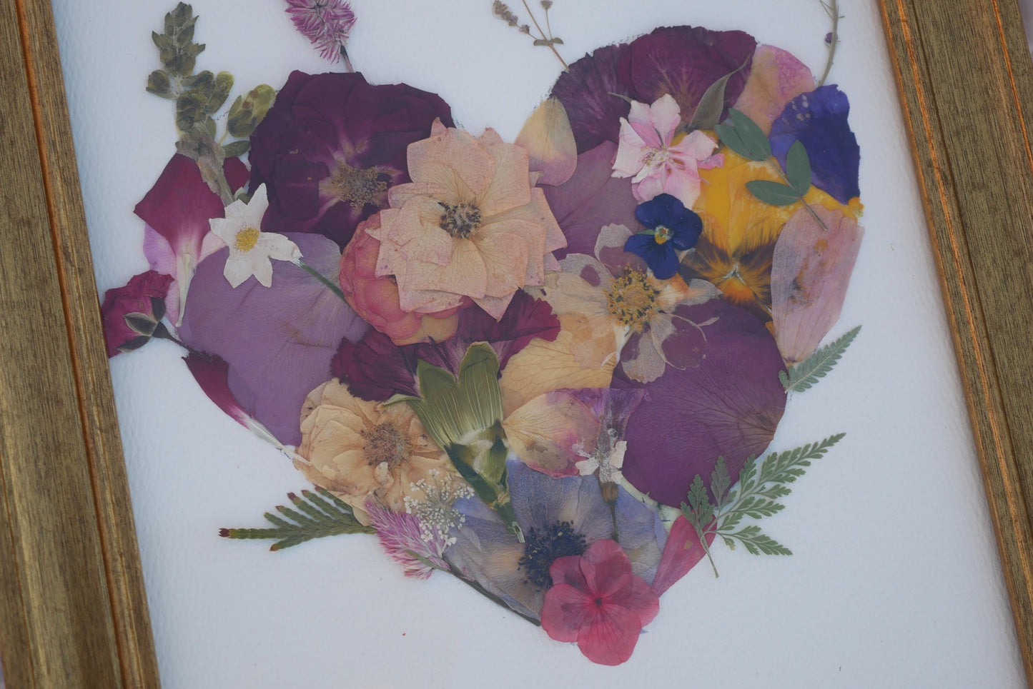 A heart-shaped arrangement of various colorful flowers, including purple, pink, yellow, and blue petals, along with green leaves, creating a vibrant and visually appealing floral design.
