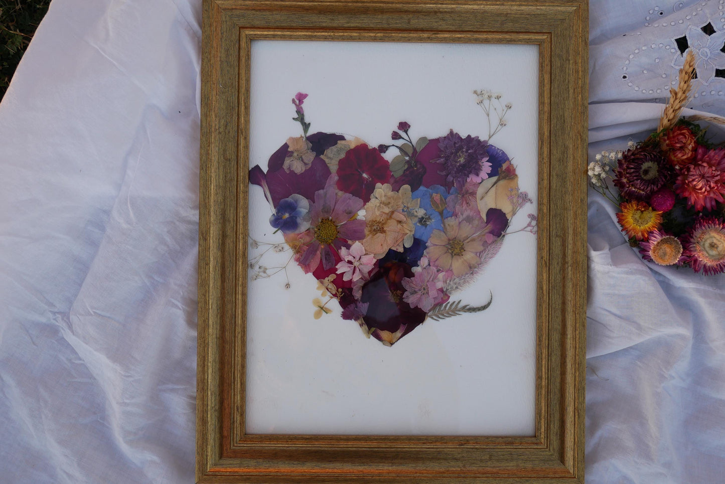 a heart-shaped arrangement of various colorful flowers, displayed in a wooden frame.