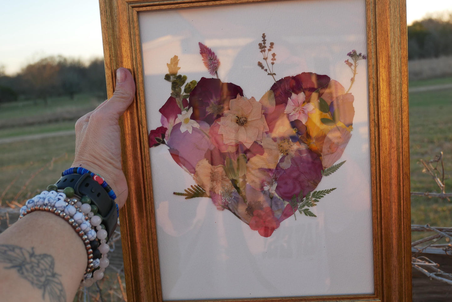 A person's hand holding a framed collage of colorful flowers and leaves, with the person's arm visible in the frame.