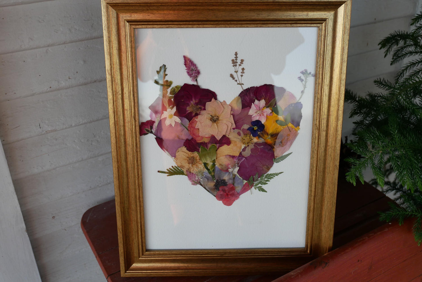 A framed collage of various colorful flowers, including roses, daisies, and other blooms, arranged in the shape of a heart.