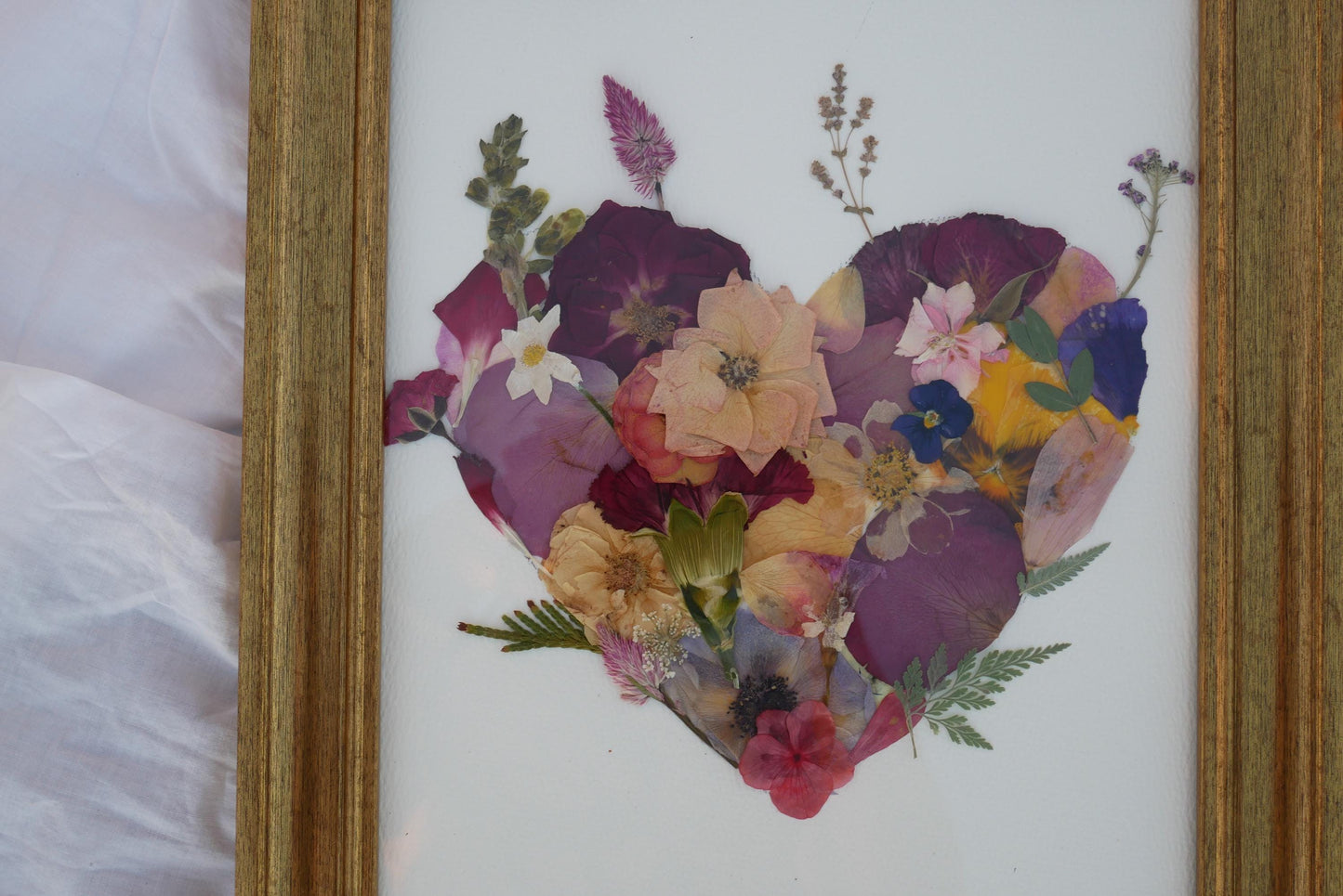 A framed collage of various colorful flowers and leaves arranged in the shape of a heart.