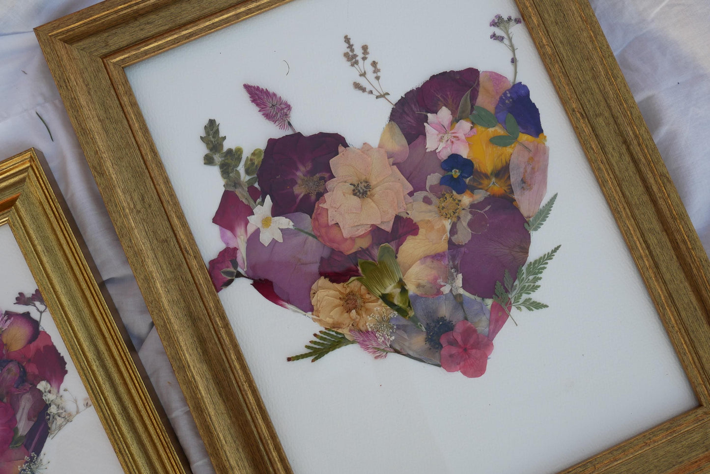 a framed collage of various flowers and leaves, including a heart-shaped arrangement of flowers and leaves.