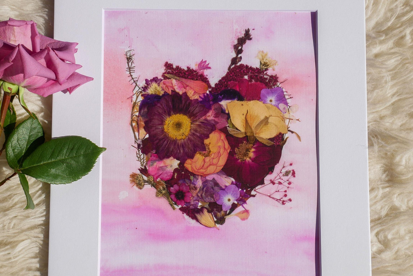 a heart-shaped arrangement of various colorful flowers, including roses, against a pink background.