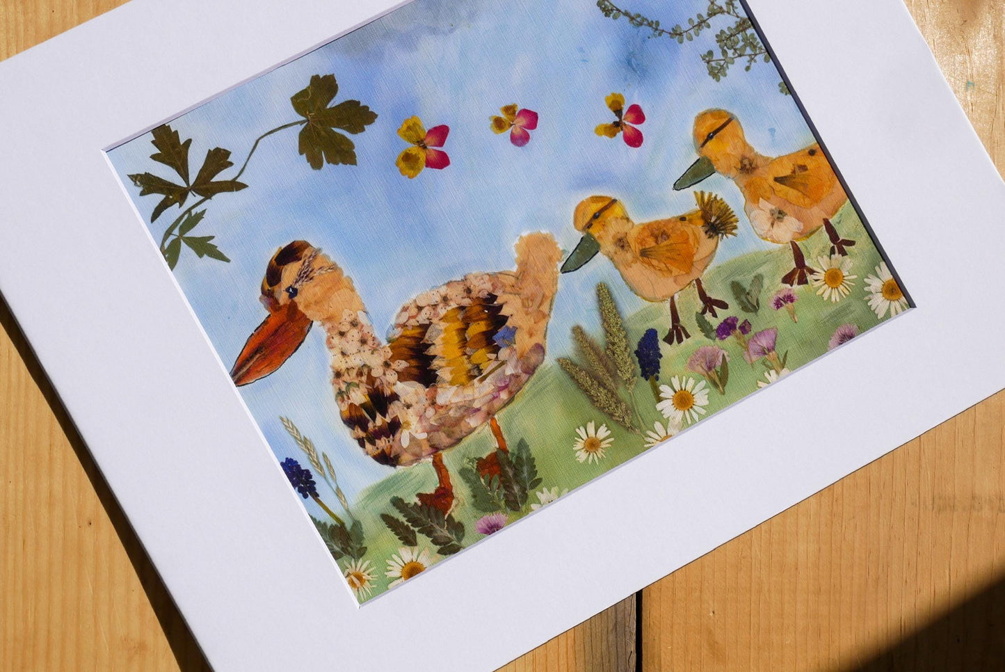 The image is a framed print depicting a vibrant scene of ducks in a field with flowers and leaves.