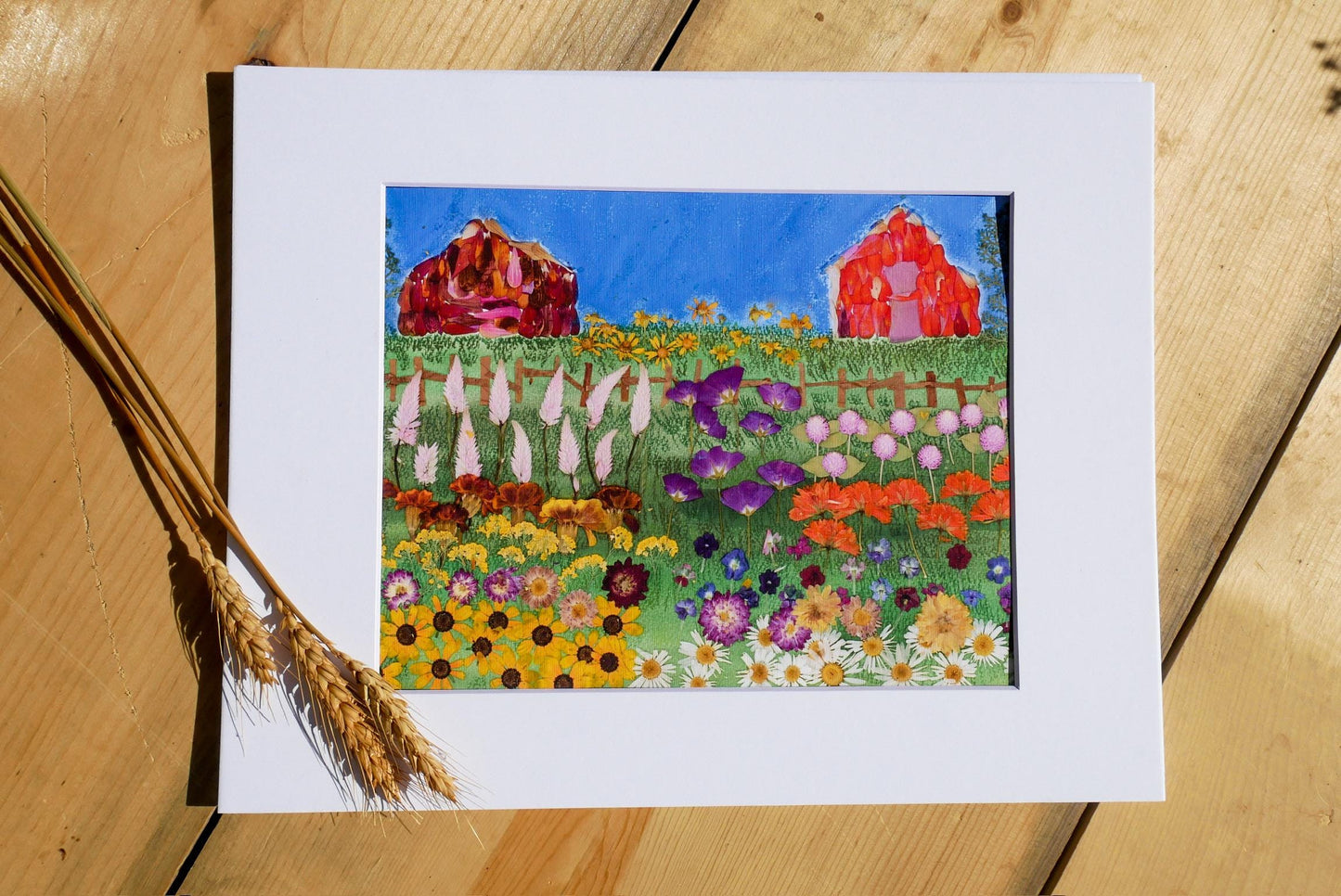 The image is a framed painting depicting a vibrant garden scene with colorful flowers, a red barn, and a wooden fence.