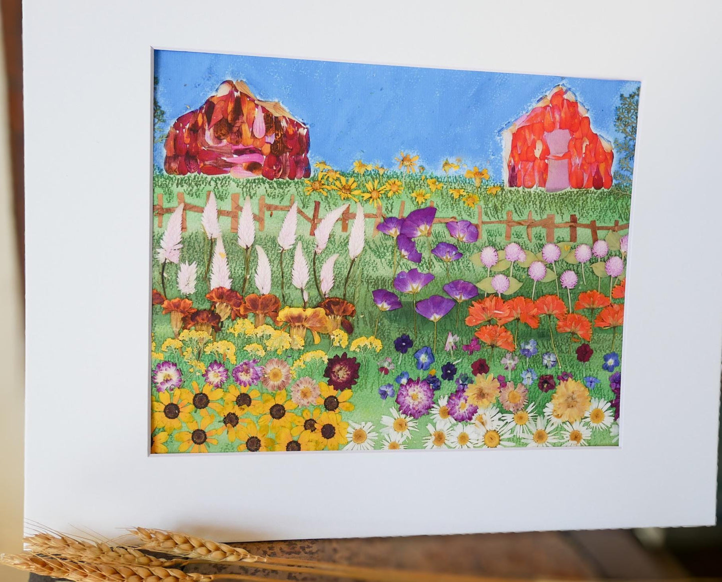The image is a vibrant painting depicting a lush garden filled with a variety of colorful flowers, including sunflowers, daisies, and other blooms. The scene is set against a backdrop of a blue sky and a red barn, creating a picturesque and serene landscape.
