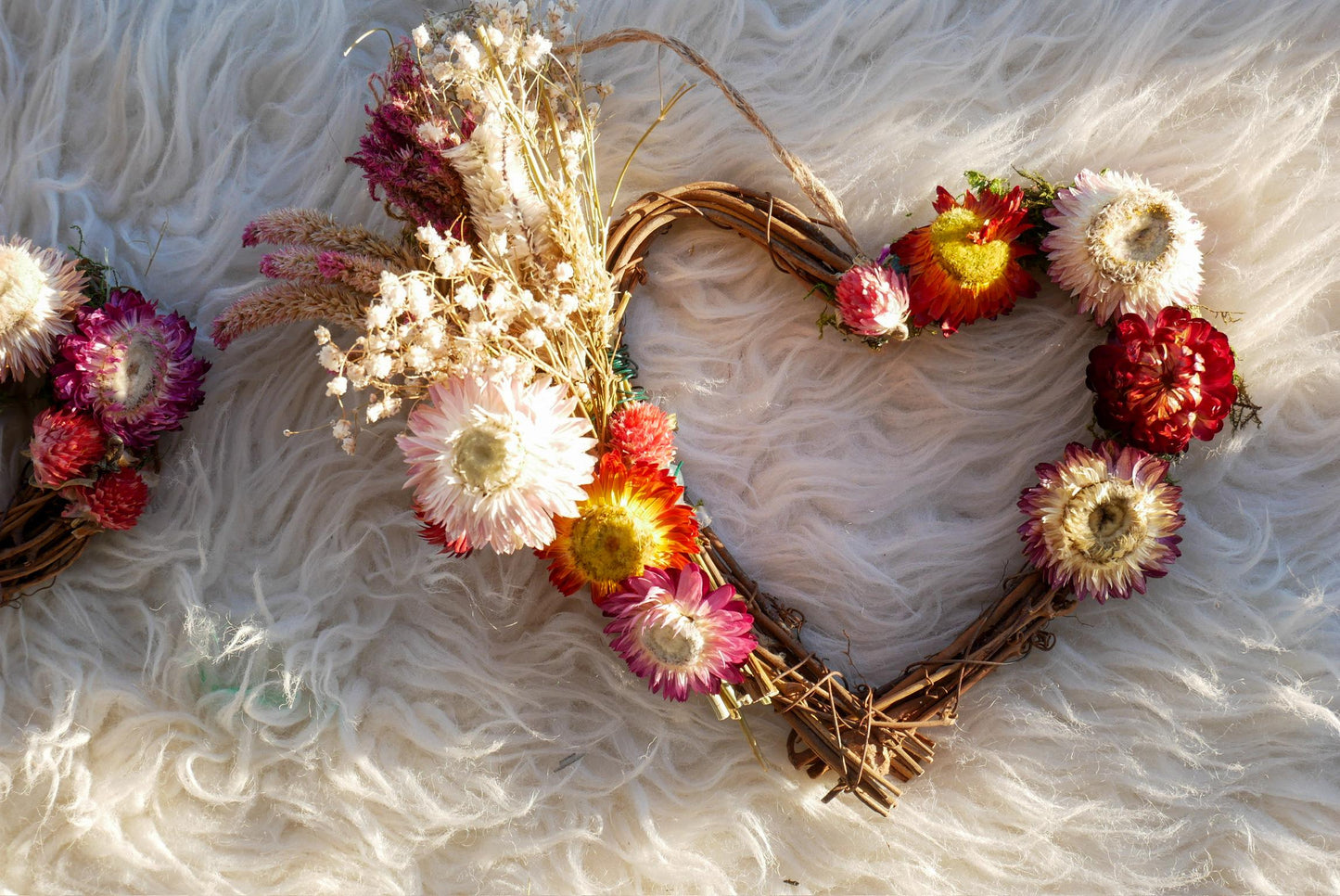 A heart-shaped wreath made of dried flowers and twigs, with a variety of colorful flowers including red, pink, and yellow blooms.