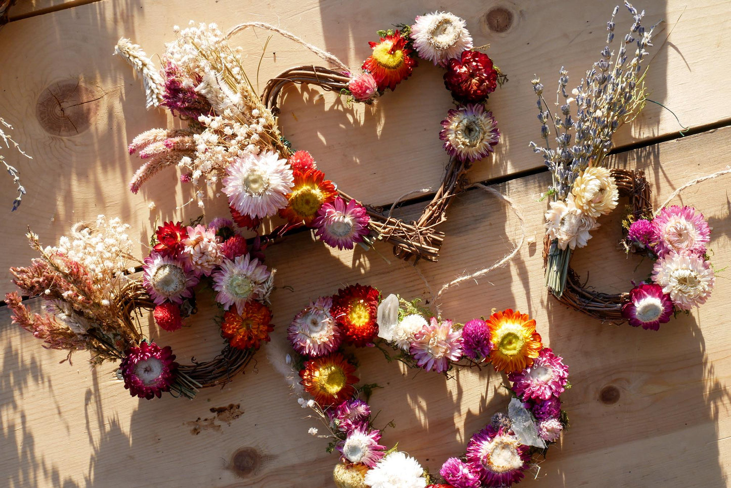 a collection of wreaths made from dried flowers and branches, arranged on a wooden surface.
