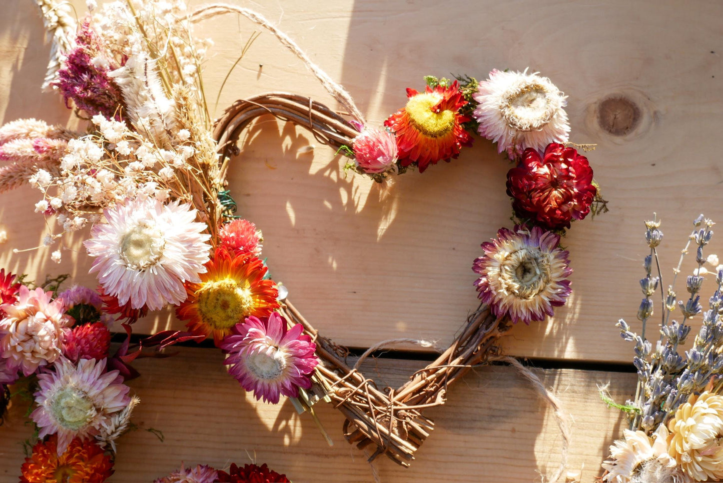 A heart-shaped wreath made of dried flowers and twigs, with a variety of colorful flowers including red, pink, white, and yellow blooms.