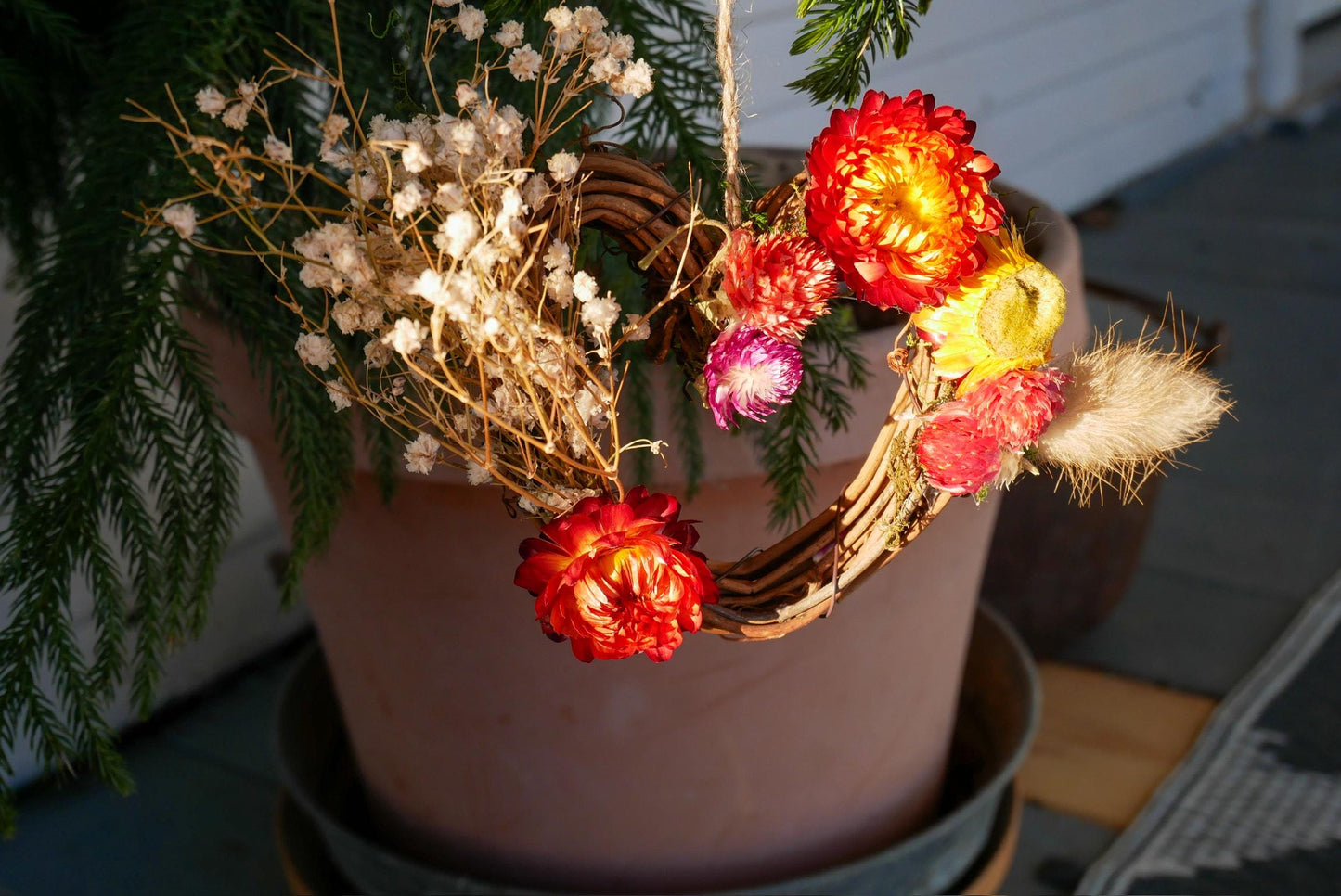 A terracotta pot filled with dried flowers and greenery, placed on a wooden surface.