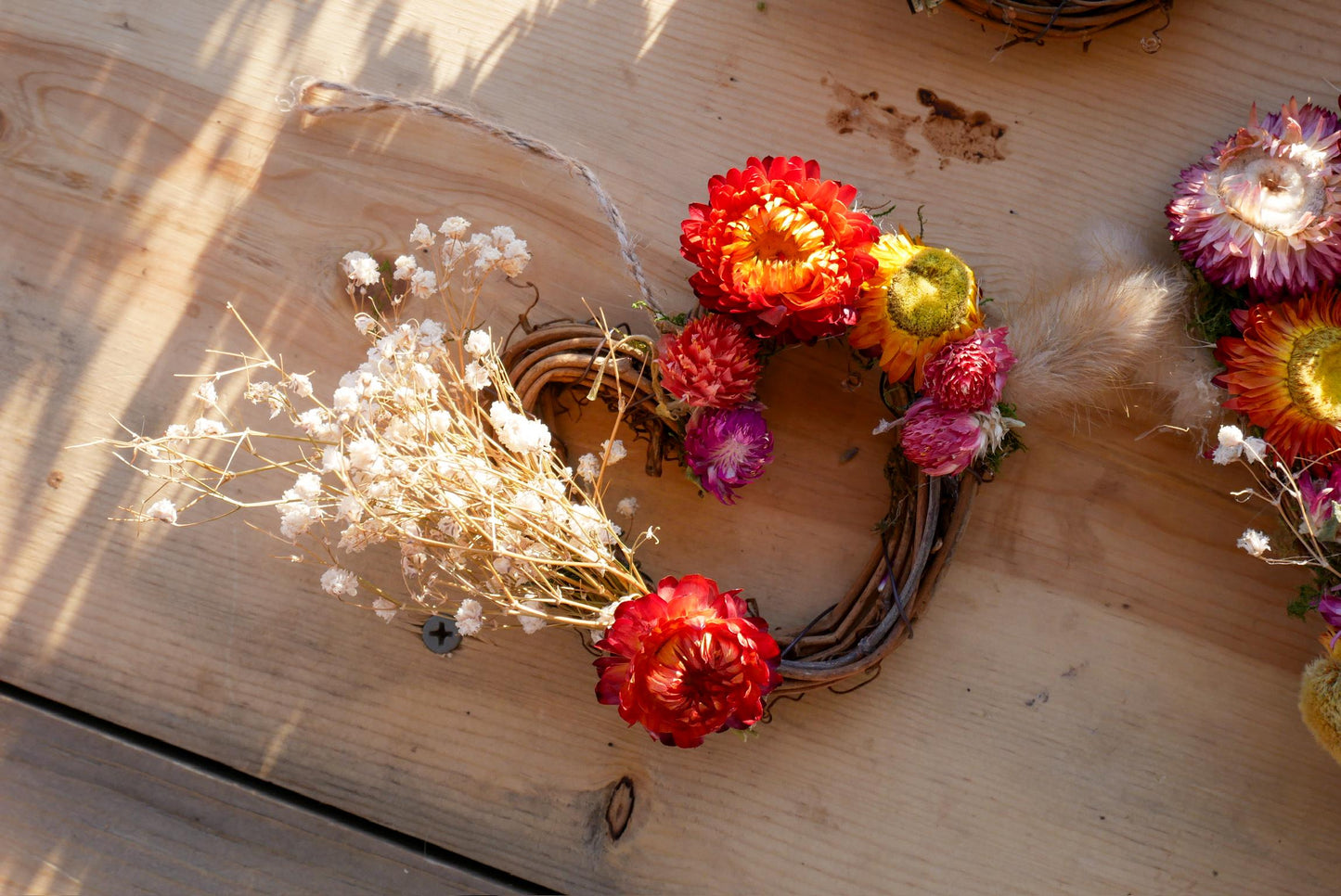 A wreath made of dried flowers and twigs, with a variety of colors including red, orange, yellow, and white.