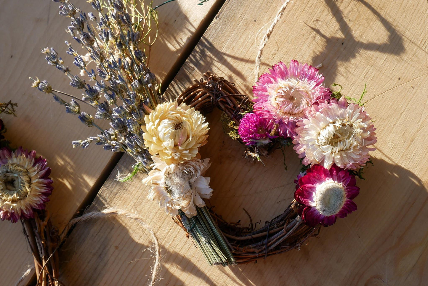 A wreath made of dried flowers, including purple and white flowers, is displayed on a wooden surface.