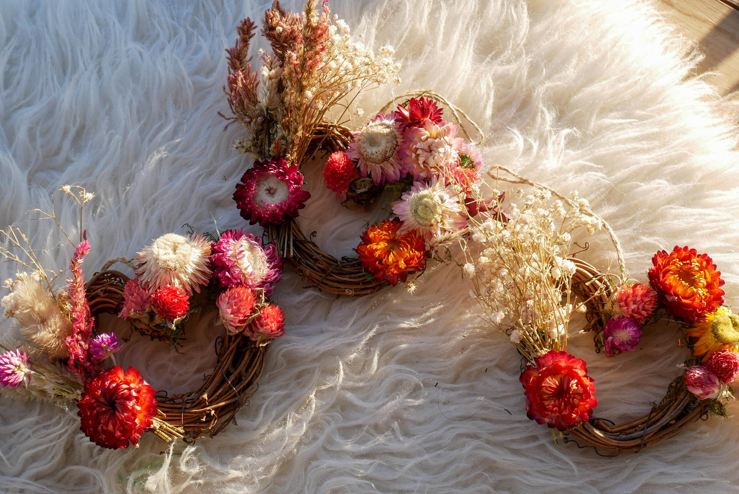 A wreath made of dried flowers and branches, with a variety of colors including red, orange, yellow, and white.
