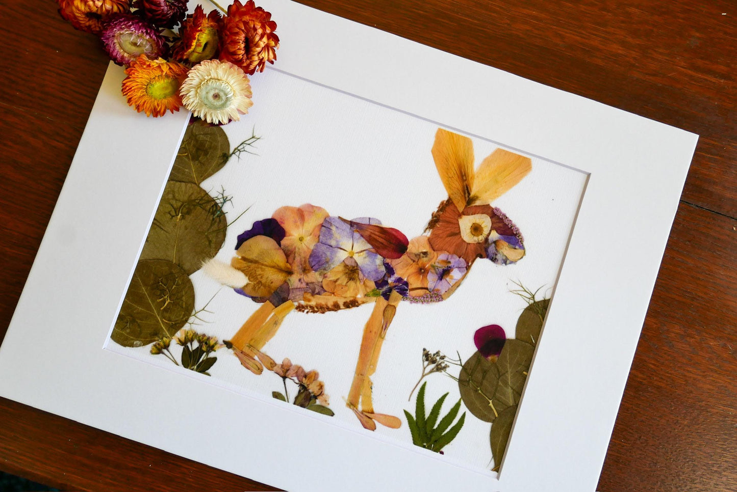 a framed artwork depicting a colorful rabbit made entirely of dried flowers and leaves, set against a natural backdrop.