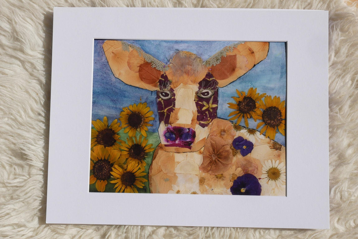 A collage of a cow surrounded by sunflowers and other flowers, with a white frame.