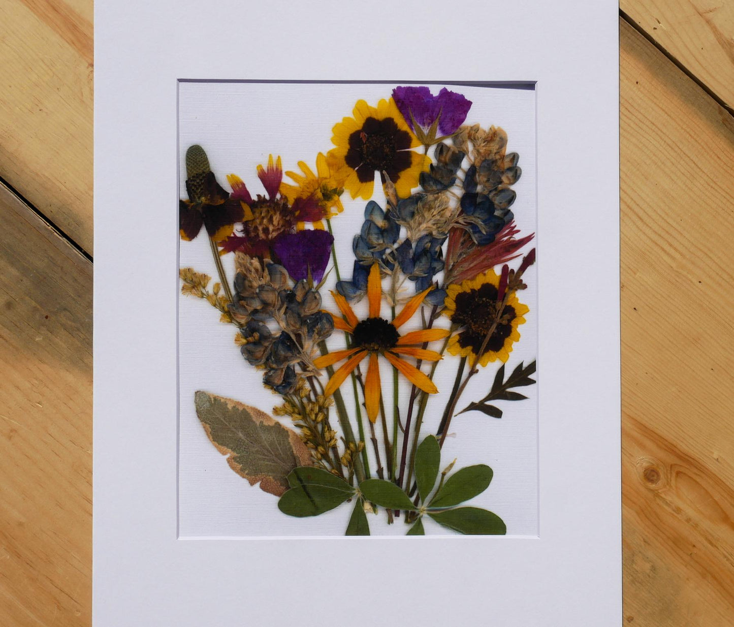 A framed arrangement of dried flowers and leaves, showcasing a vibrant and colorful floral display.
