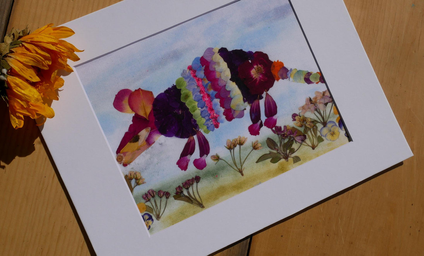 A framed artwork depicting a colorful, abstract representation of a flower or plant, with various shades of purple, pink, and green.