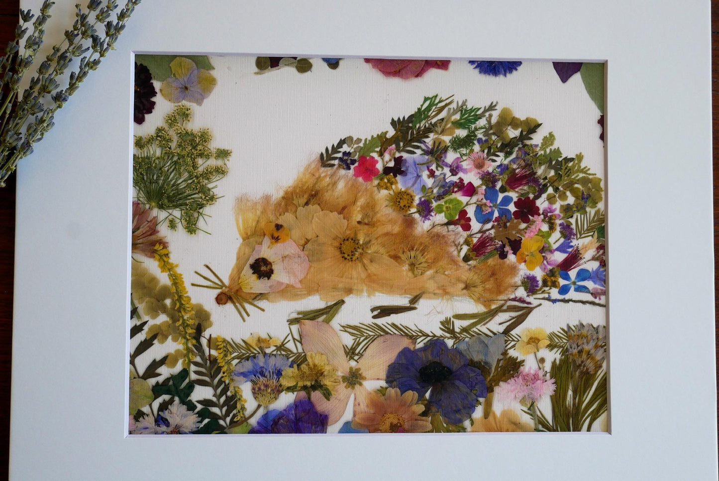 The image is a framed collage of various colorful flowers and leaves, including a hedgehog-like creature made of pressed flowers.