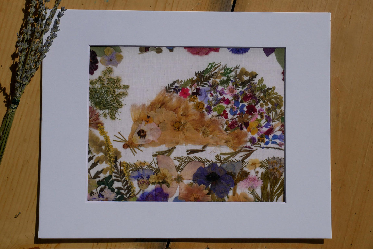 The image is a framed print featuring a vibrant arrangement of flowers and leaves, including a hedgehog-like creature, all set against a white background.