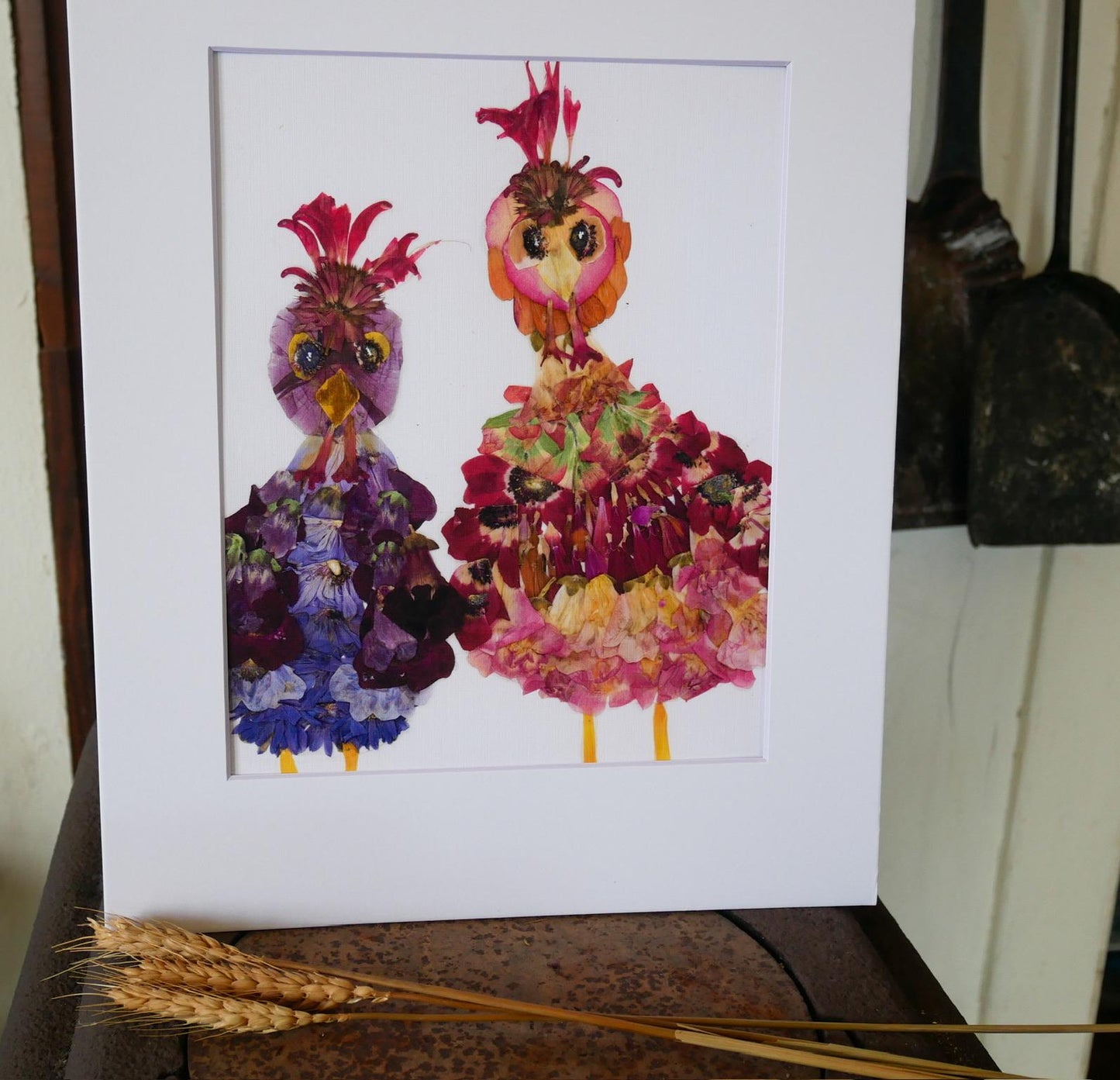two colorful bird-like figures made from flowers, with one figure wearing a red and yellow outfit and the other in a purple and pink outfit.
