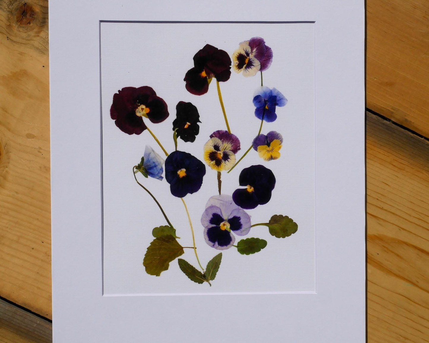 The image is a framed print featuring a close-up view of a variety of colorful flowers, including purple, blue, and yellow blooms.