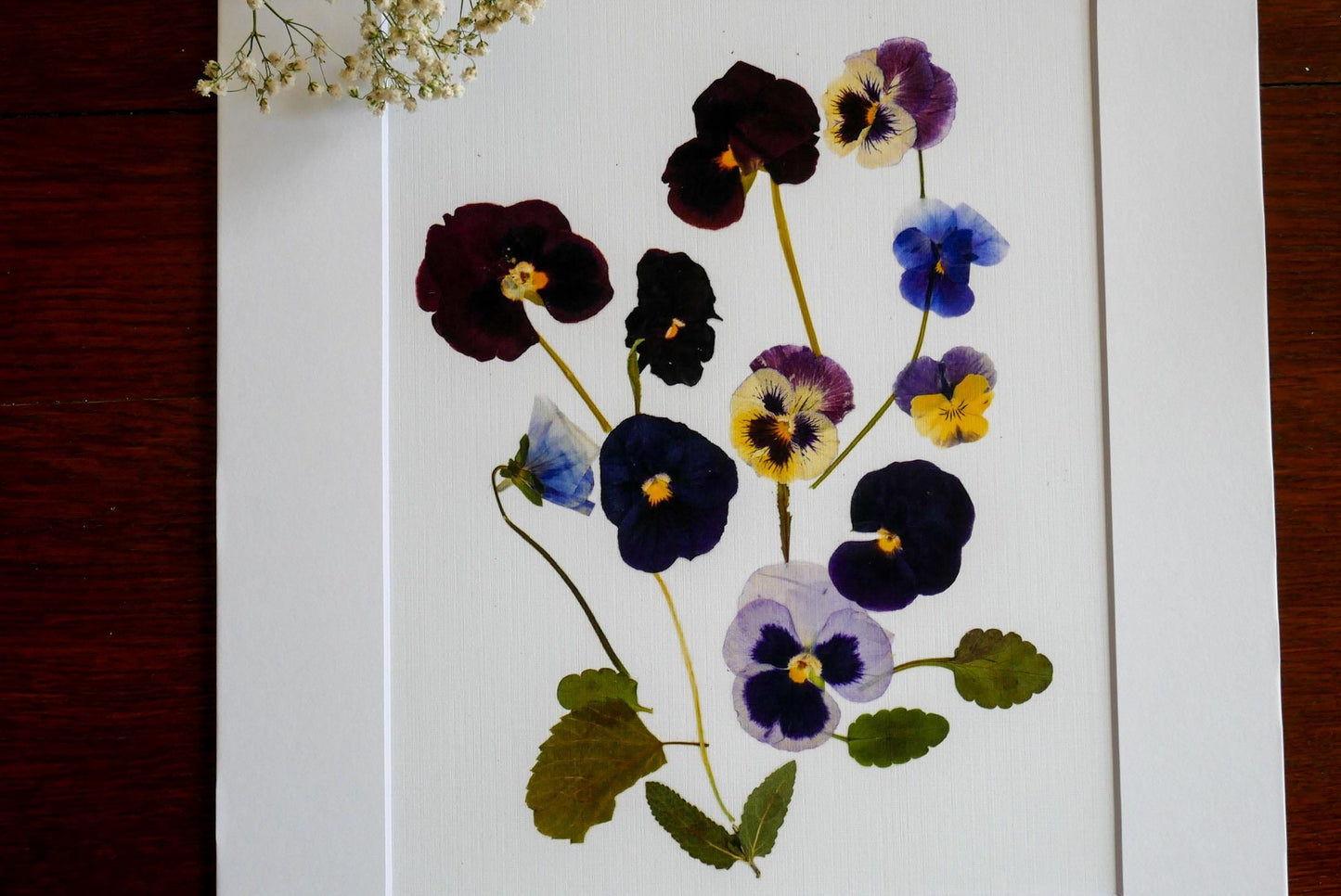 a close-up view of a white frame containing a vibrant arrangement of colorful flowers, including purple, blue, and yellow pansies.