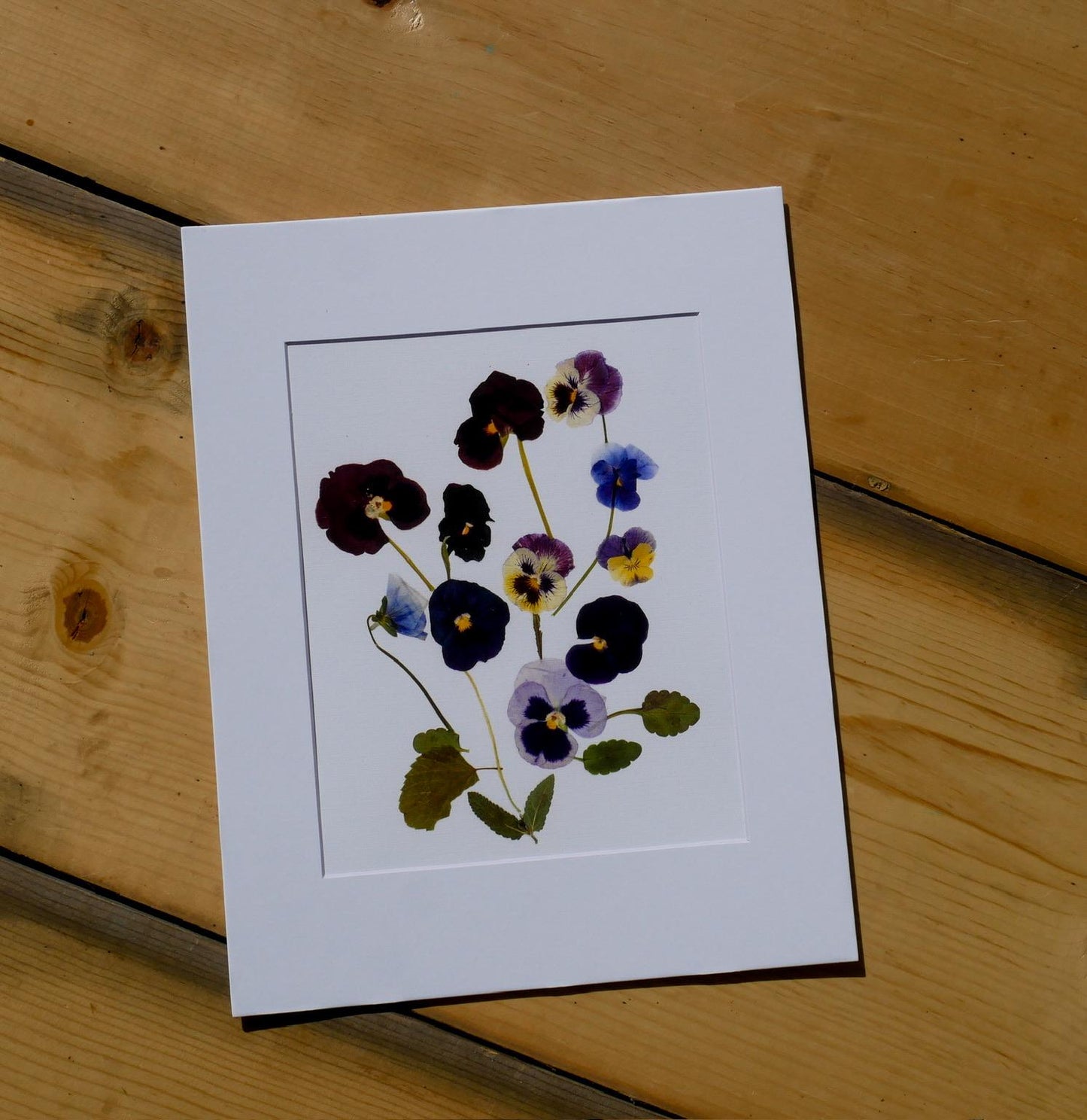 A framed image of dried flowers is placed on a wooden surface.
