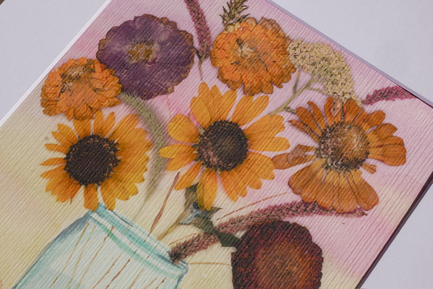 A close-up of a vibrant bouquet of sunflowers and other flowers, with a textured pink background.