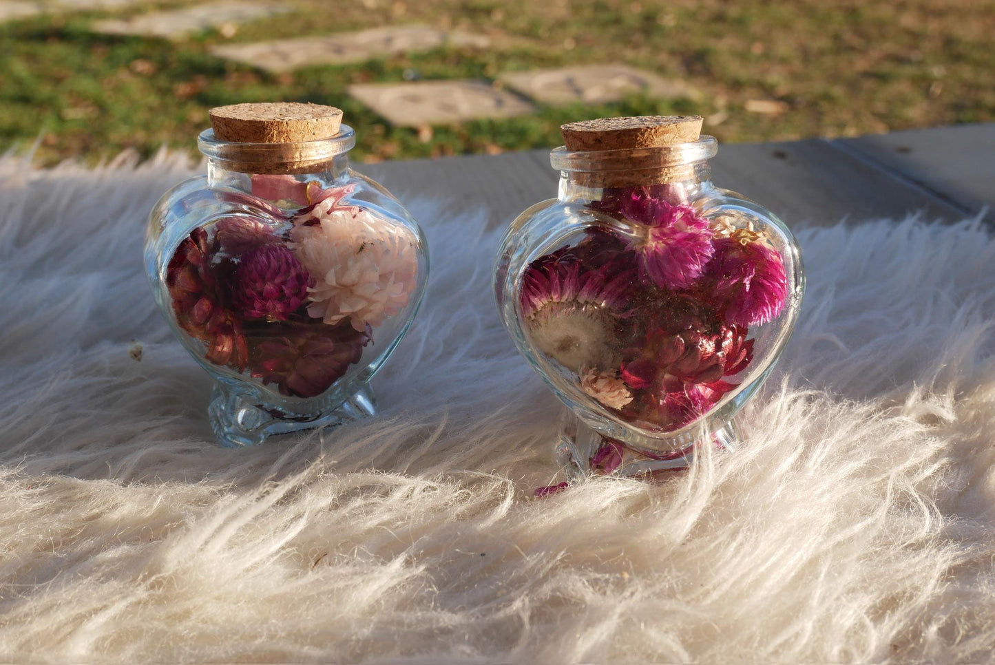 Two glass jars filled with colorful flowers, including pink and purple petals, sit on a white furry surface.