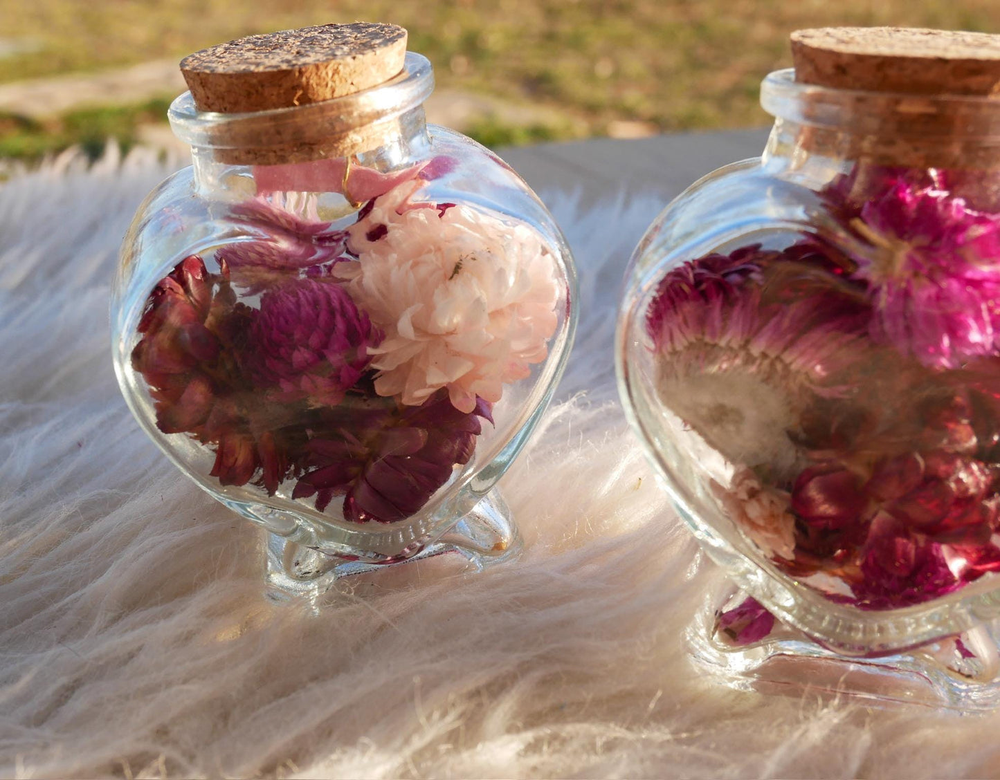 Two glass jars filled with colorful flowers, placed on a white fur surface.