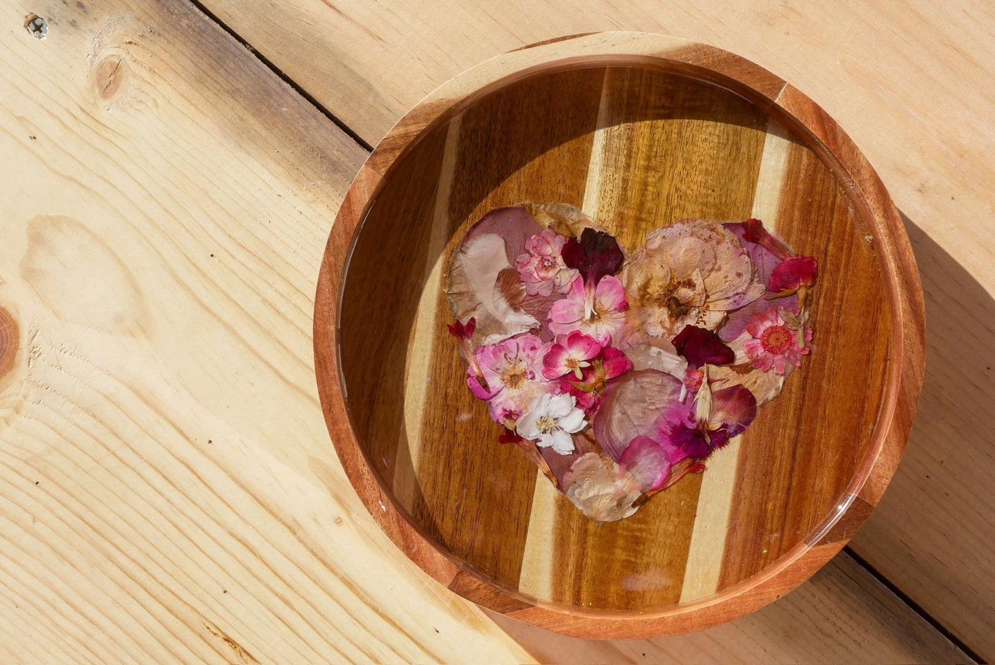 A wooden bowl filled with pink and white flower petals arranged in the shape of a heart.