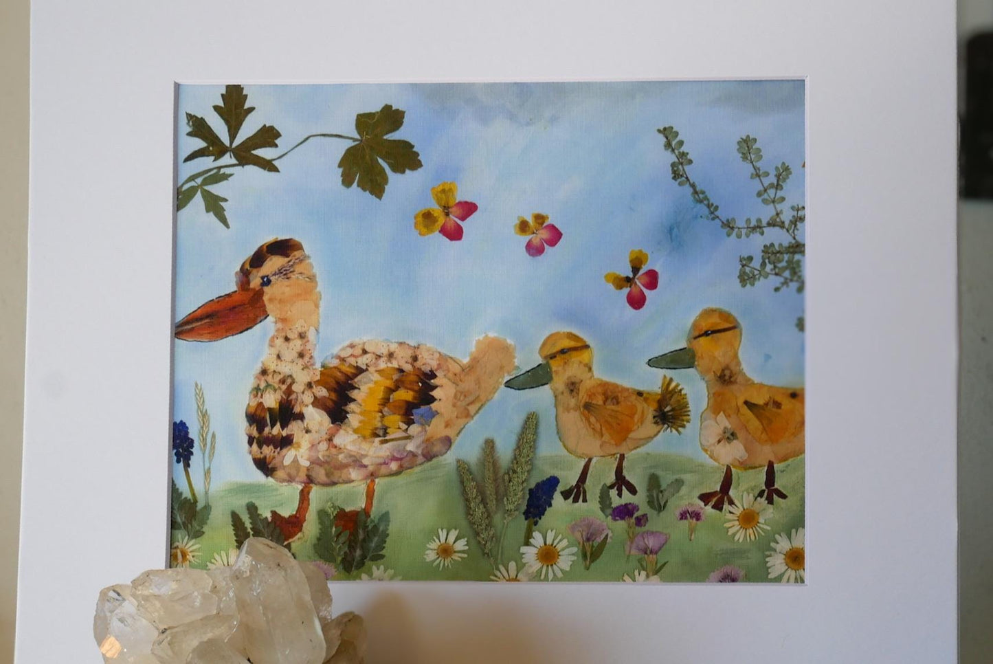 The image is a collage of various elements, including a large bird, smaller birds, flowers, leaves, and a crystal.