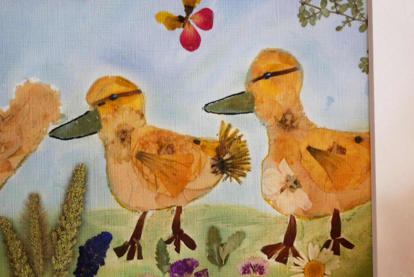 The image is a collage featuring two yellow ducks surrounded by various flowers and plants, including a red flower, a yellow flower, and a purple flower.