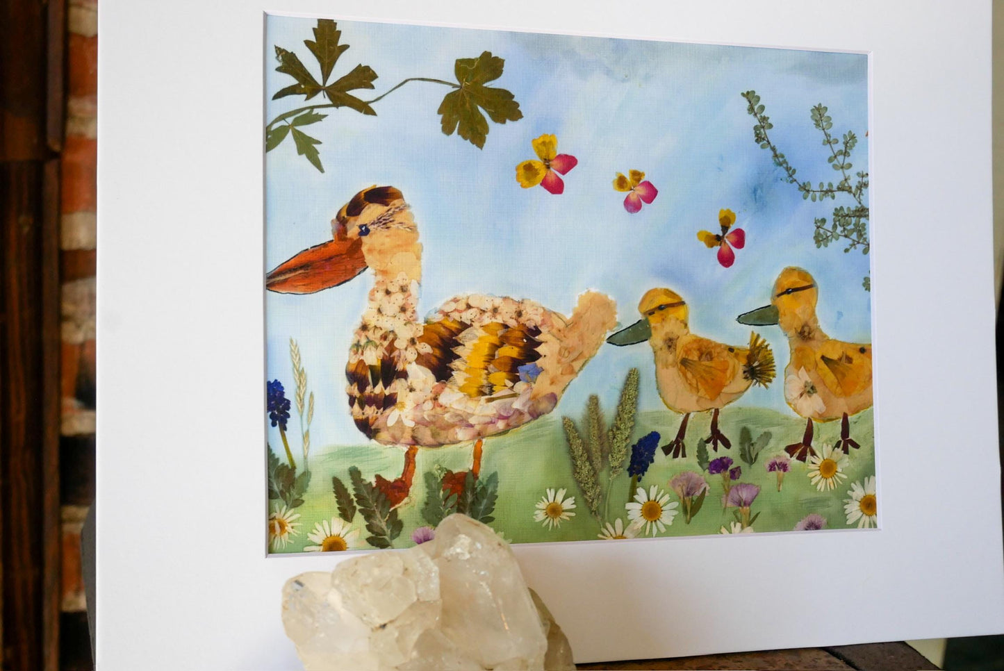 The image is a collage of various natural elements, including a duck, flowers, leaves, and butterflies, all set against a blue sky background.