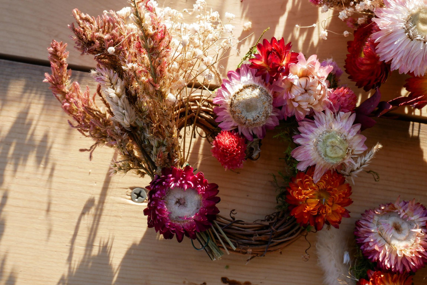 A wreath made of dried flowers and greenery, with a variety of colors including red, pink, orange, and white.